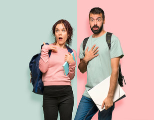 Two students with backpacks and books surprised and shocked. Expressive facial emotion on colorful wall