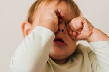 Sleepy baby rub her eyes. CLose up portrait of tired toddler