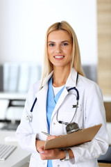 Doctor woman at work in hospital excited and happy of her profession. Blonde physician controls medication history records and exam results while using clipboard. Medicine and healthcare concept