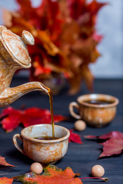Morning coffee in mugs and a coffee pot pours coffee in a mug on a dark wooden background with maple leaves