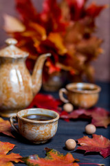 Morning coffee in mugs and coffee pot on a dark wooden background with maple leaves
