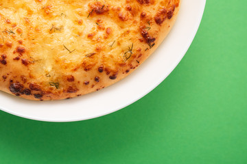 Fresh round cake on white plate on green background.