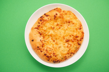 Fresh round cake on white plate on green background.