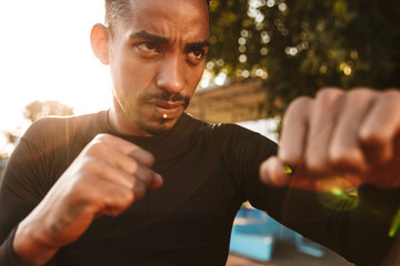 Image of african american man clenching fists and boxing on sports ground