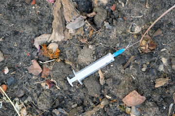A white syringe lies on the ground top view. Used syringe with an open needle. The problem of addiction and addiction. Danger of infection.