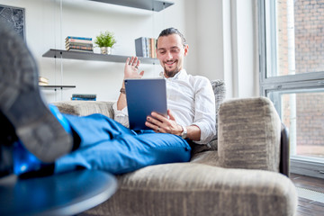 Photo of businessman sitting on sofa with tablet in his hands in room.