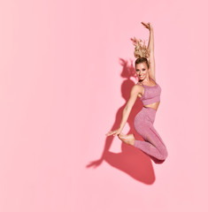 Happy athletic woman jumping in silhouette. Photo of sporty woman in fashionable pink sportswear on pink