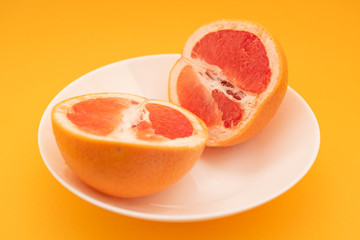 Obraz na płótnie Canvas Fresh ripe juicy grapefruit on white plate on yellow background.