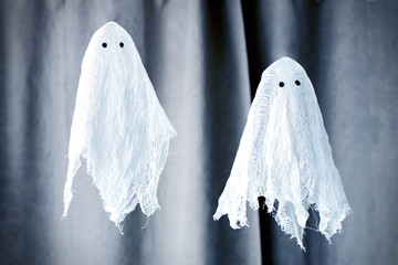 Two toy white ghosts made of gauze on the background of the curtains