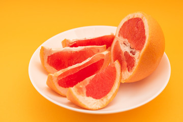 Fototapeta na wymiar Fresh ripe juicy grapefruit on white plate on yellow background.