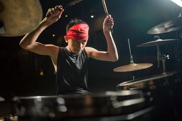 young boy as rock band drummer . Handsome and cool Asian American teenager in headband playing drum...