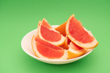 Fresh ripe juicy grapefruit on white plate on green background.