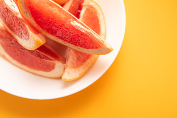 Naklejka na ściany i meble Fresh ripe juicy grapefruit on white plate on yellow background.