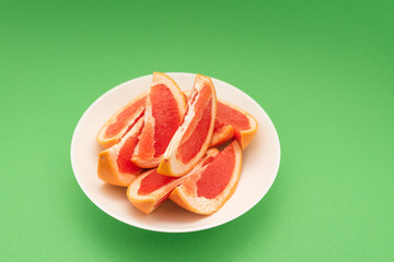Fresh ripe juicy grapefruit on white plate on green background.
