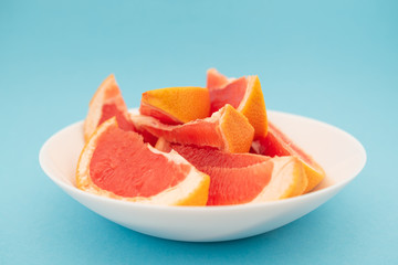 Fresh ripe juicy grapefruit on white plate on blue background.