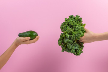 Healthy vegetables for kids. Kid hand with bunch of kale leaves and kid hand holding avocado over...