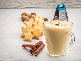 Eggnog with cookies, cinnamon, nutmeg on a white wooden table.