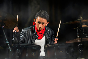 13 or 14 years old cool and talented Asian American mixed ethnicity boy playing drums in leather jacket and bandana  practicing and performing song