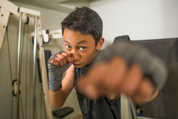 Asian American teenager boxing on gym . Portrait of young handsome and fierce 13 or 14 years old boy in wrist wraps doing fight workout looking cool in tough attitude