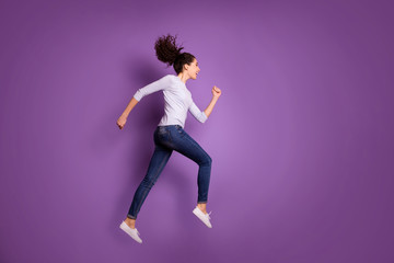 Full length body size photo of cheerful cute charming nice sporty woman wearing jeans denim sneakers running for sales with hair blown thrown jumping isolated pastel color background