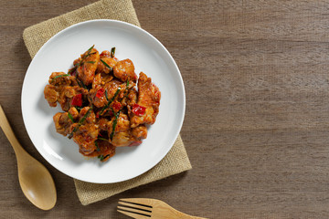 top view of stir fried chicken with red curry paste in a ceramic dish on wooden table. hot and spicy thai style food menu.
