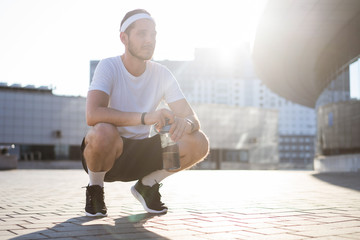 Fototapeta na wymiar Young athlete in windrunner sitting on the street after good jogging session at sunset.