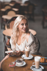 Beautiful blonde girl 20-24 year old sitting in cafe reading paper book drinking coffee outdoors closeup. Good morning. Breakfast time.