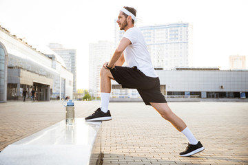 Young male jogger athlete training and doing workout outdoors in city.