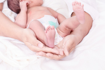 Selective focus mother hands hold her tiny bare feet newborn daughter with carefully