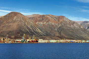 View of the small northern port town of Egvekinot, located on the shore of the Kresta Bay of the Bering Sea. Landscape with a seaport and buildings on a background of mountains. Chukotka, Russia.