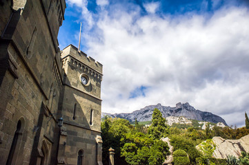 Wall and clock tower of an old stone castle on a background of mountains and sky