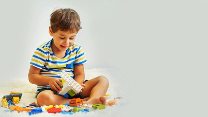 happy asian boy playing with colorful construction plastic blocks on white Bed at home.