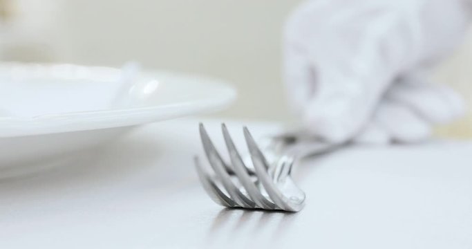 Mano con guanto di un cameriere che sta apparecchiando la tavola di un ristorante