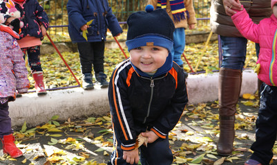 Little smiling child with yeallow leaf in the kindergarden in autumn