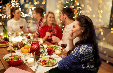 holidays, communication and celebration concept - happy young woman calling on smartphone and having christmas dinner with friends at home