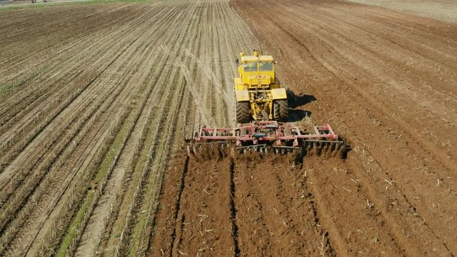 Tractor with disc harrows on farmland, top view. Tractor cuts furrows in a plowed field. Preparing the field for planting vegetables. Agricultural work with a tractor.