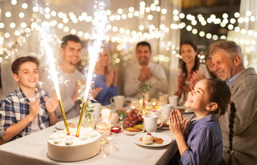 celebration, birthday and people concept - happy family having dinner party with fountain fireworks...