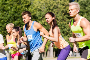 fitness, sport, race and healthy lifestyle concept - group of people or sportsmen with badge numbers on start of running marathon at summer park