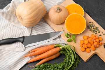 food, culinary and vegetable concept - cut pumpkin, carrots, linen towel and kitchen knife on table