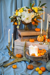 Bronze vase in which stands a bouquet of lily flowers, a peony rose, eustoma and green leaves with persimmons and red berries. Flowerpot on a white box, orange pumpkins, autumn mood. Luxury Wedding.