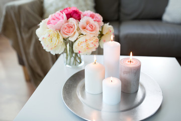 decoration, hygge and cosiness concept - candles burning on table and flowers at cozy home