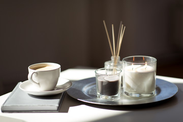 hygge and aromatherapy concept - coffee, candles, book and aroma reed diffuser on table