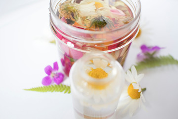 glass bottle oil based on various medicinal herbs and flowers, cosmetic oil for skin care on white background