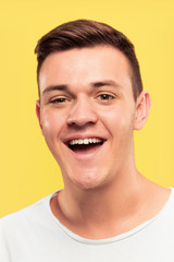 Fototapeta premium Caucasian young man's close up portrait on yellow studio background. Beautiful male model with well-kept skin. Concept of human emotions, facial expression, sales, ad. Smiling, laughting.