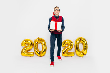 A little boy in a Santa hat, a stylish child with a Christmas gift in his hands, on a white...