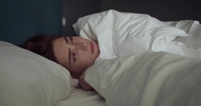 Beautiful redhead woman awakening without mood in cozy bed.