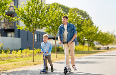 family, leisure and fatherhood concept - happy father and little son riding scooters together in city