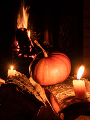 Halloween pumpkin in the dark on birch logs next to burning candles. In the background is a flame...