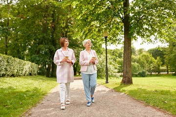old age, retirement and people concept - two senior women or friends drinking coffee walking along...