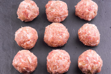 Nine raw meatballs on a dark slate background close-up